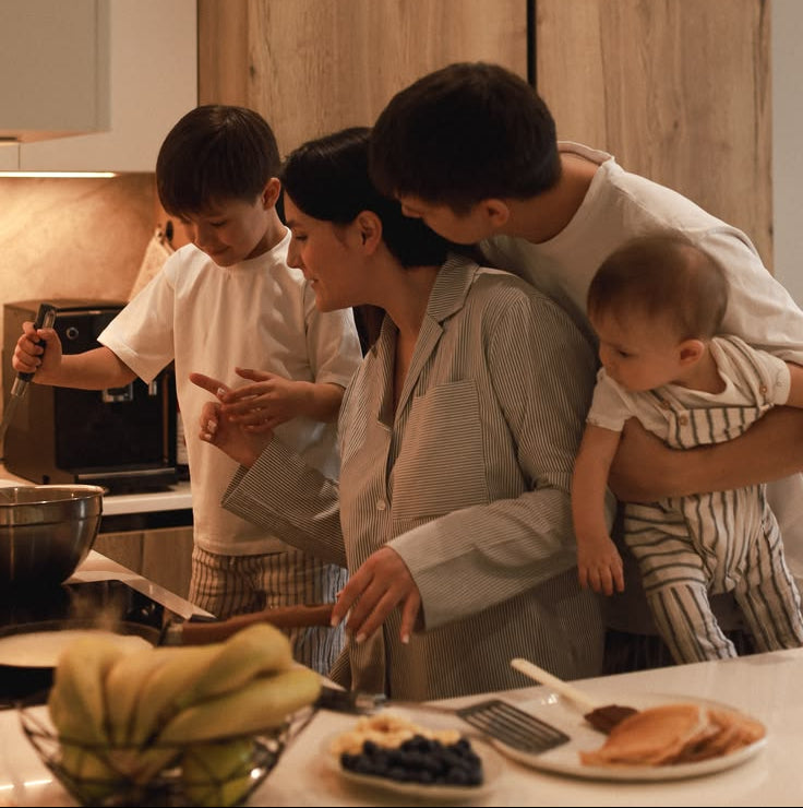 Family in a kitchen with a child using a microwave, another child being held, and a woman preparing food.